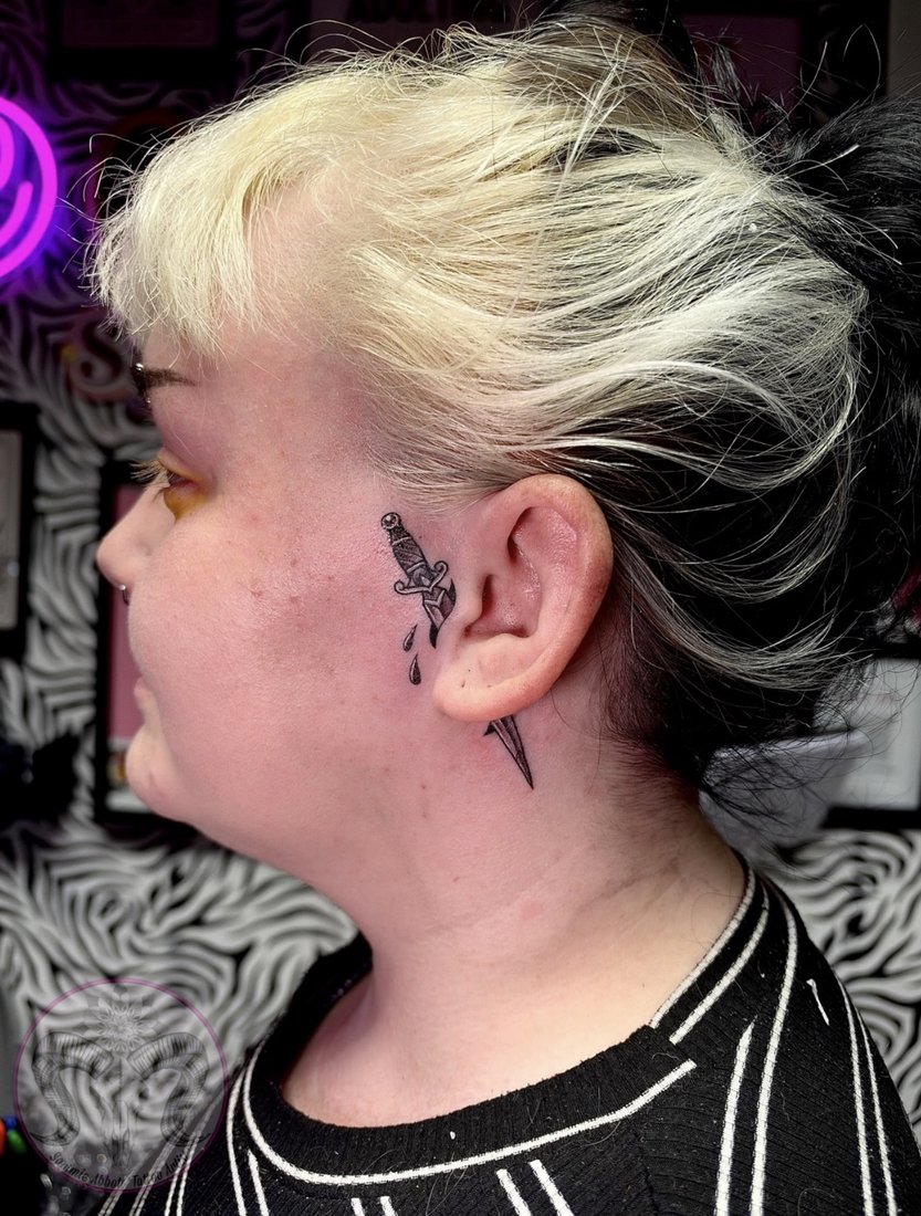 Small fine line dagger tattoo behind the ear