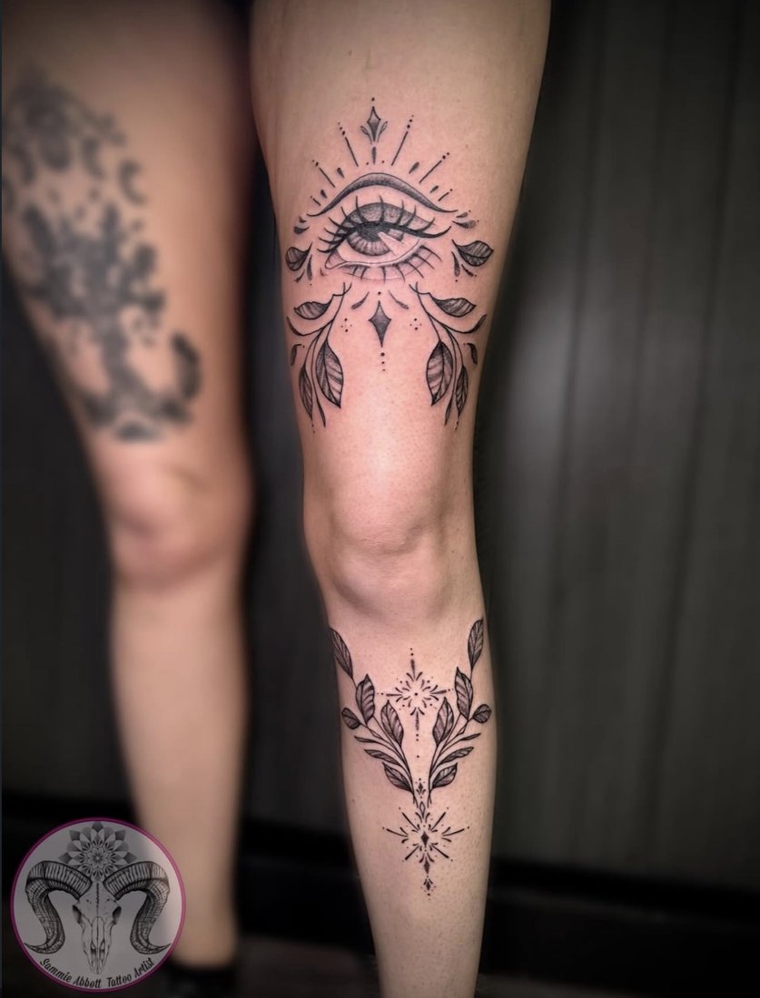 Ornamental eye and leafwork tattoo across the thigh and shin